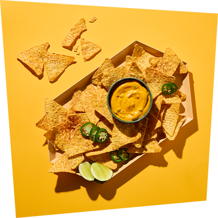Ein Teller voller knuspriger Nachos und in der Mitte eine Dip Schüssel mit der Nacho Sauce von Develey