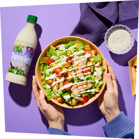 Eine Schüssel frischer Caesar Salat mit Hähnchen und Croutons, garniert mit cremigem Caesar Dressing von Develey