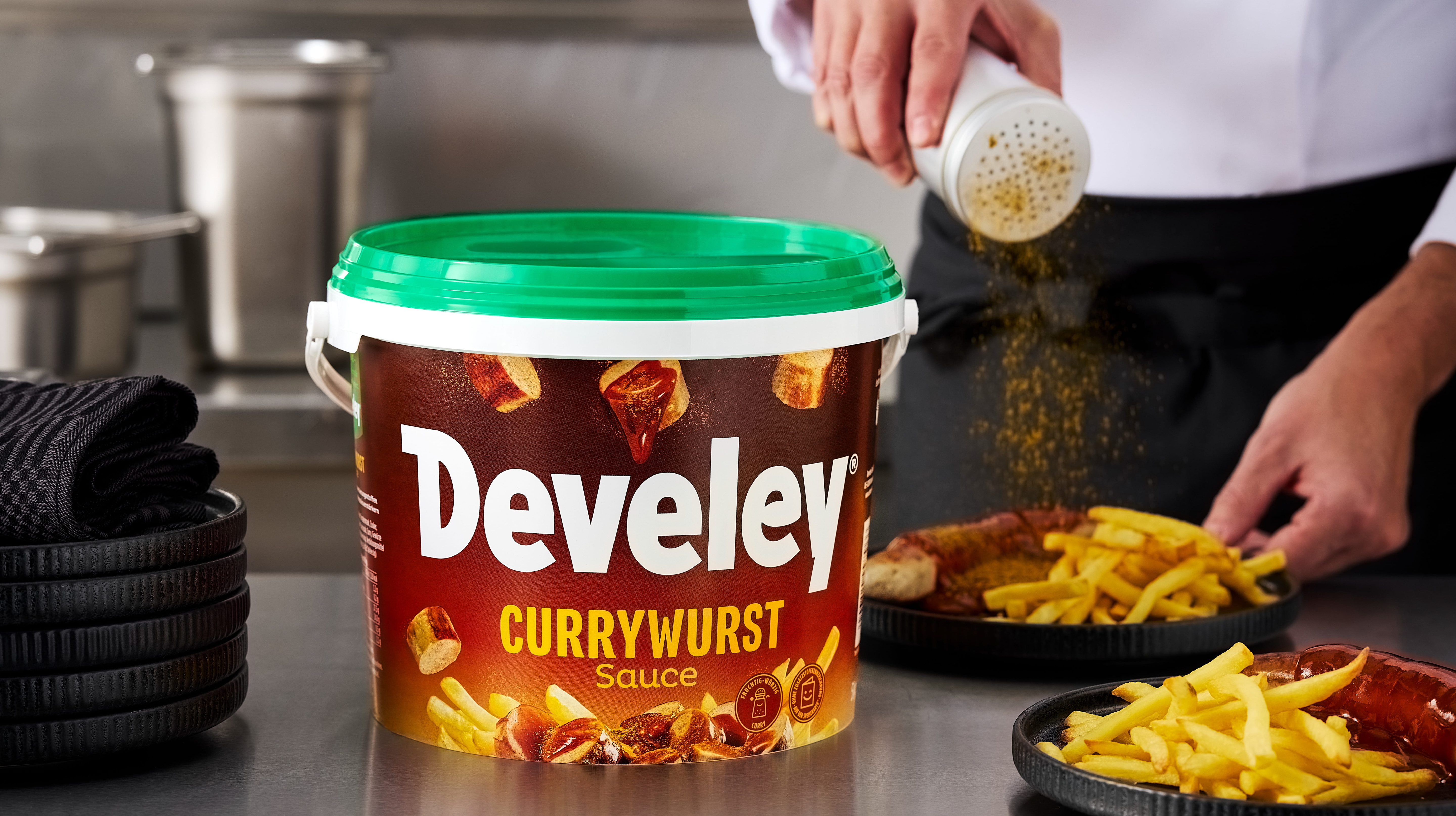 Ein Teller Currywurst mit Pommes und der würzigen Currywurst Sauce von Develey im Eimer